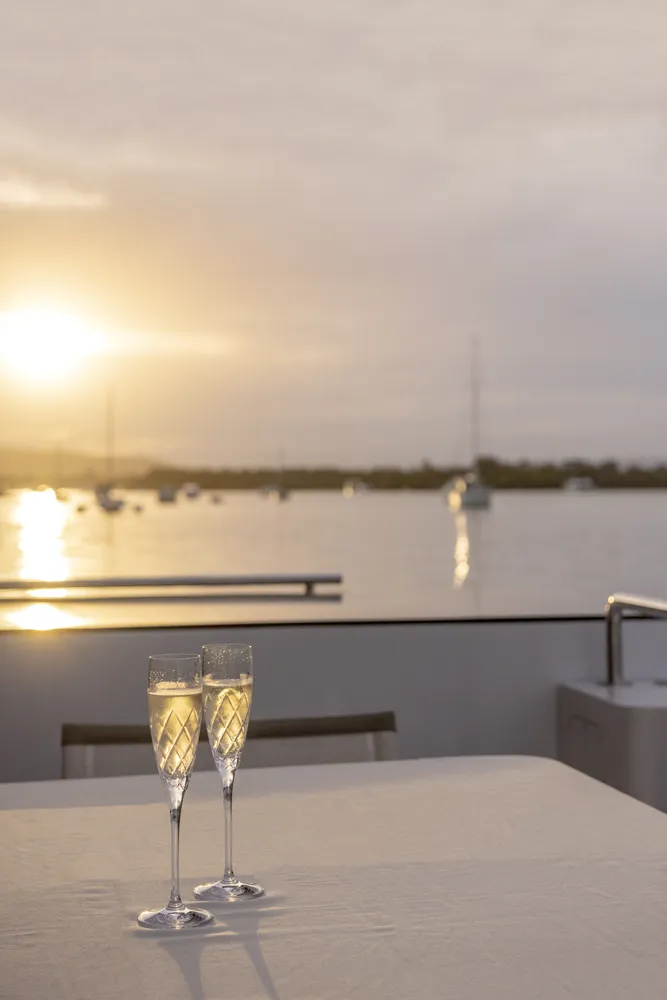 Exterior deck aerial view of a houseboat built by Mason Marine Industries, with two glasses of champagne on the table, showing the river landscape behind
