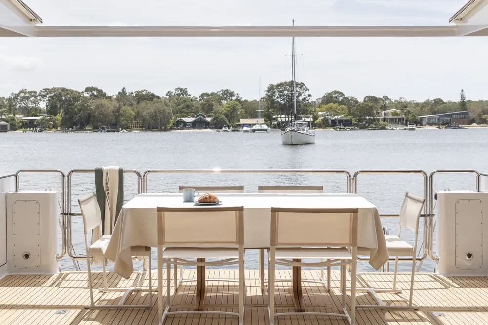 Exterior deck aerial view of a houseboat built by Mason Marine Industries, with a croissant and coffee on the table, showing the river behind