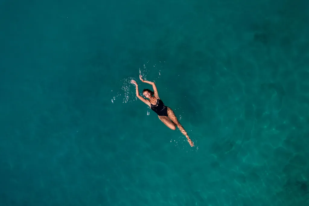 Aerial view of a lady wearing a black one-piece swimsuit, swimming in the ocean